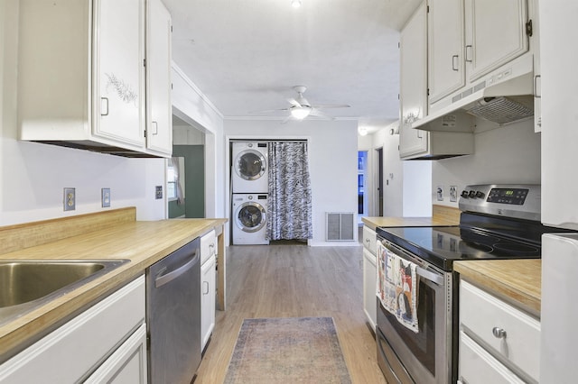 kitchen with stainless steel appliances, white cabinetry, stacked washer / drying machine, and light hardwood / wood-style floors