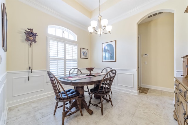 dining space with arched walkways, a raised ceiling, ornamental molding, a chandelier, and a decorative wall