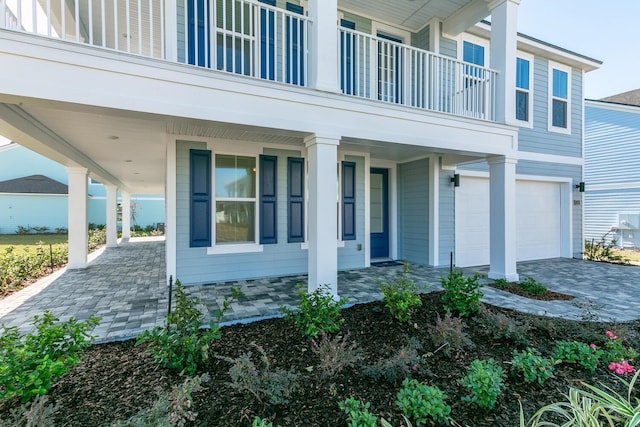 view of exterior entry featuring a porch, a balcony, decorative driveway, and a garage