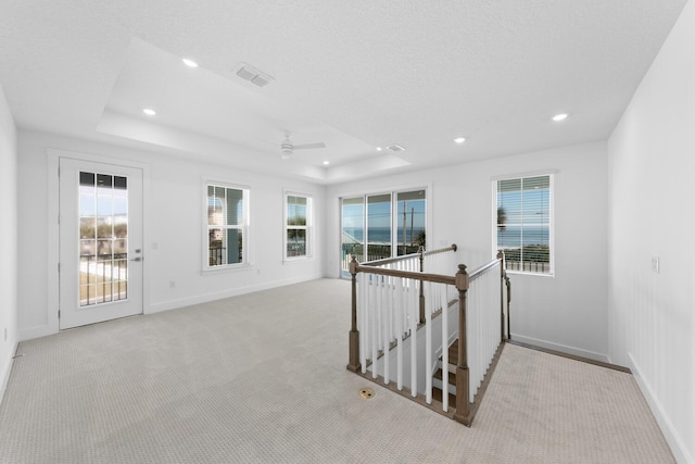 corridor with baseboards, a tray ceiling, an upstairs landing, and visible vents