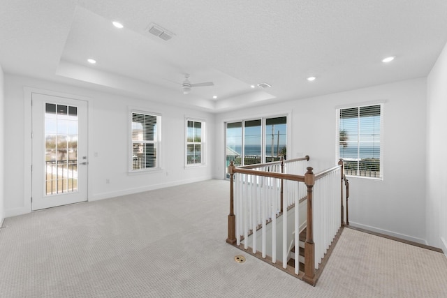 hallway with recessed lighting, a tray ceiling, an upstairs landing, and visible vents