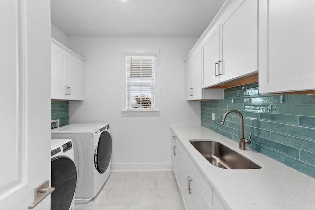 clothes washing area with washer and clothes dryer, cabinet space, baseboards, and a sink