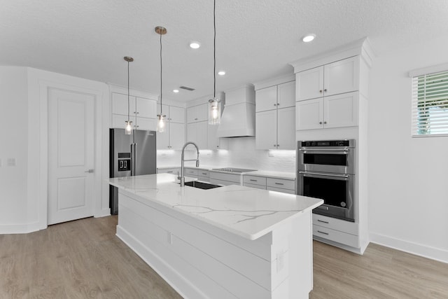 kitchen featuring premium range hood, stainless steel appliances, a sink, white cabinets, and light wood-type flooring