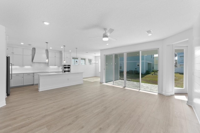 unfurnished living room with light wood-style flooring, a ceiling fan, a wealth of natural light, and a textured ceiling