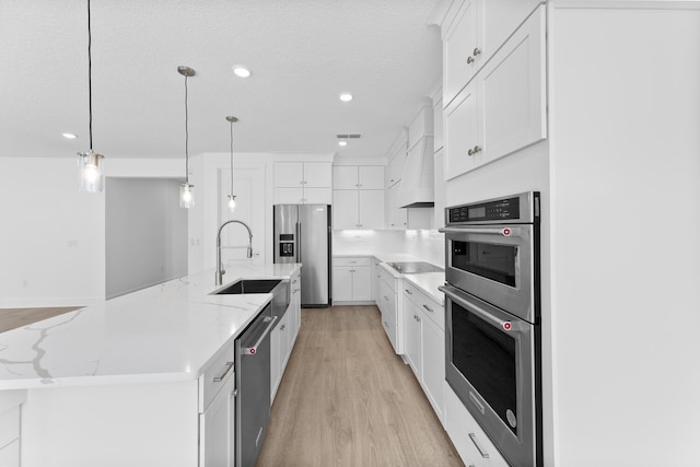 kitchen featuring a large island with sink, a sink, white cabinets, light wood-style floors, and appliances with stainless steel finishes