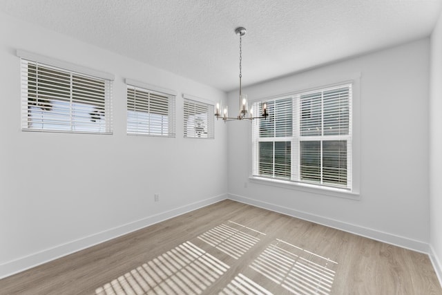 spare room with baseboards, plenty of natural light, an inviting chandelier, and wood finished floors