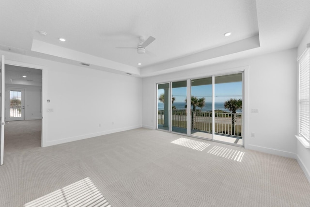 spare room featuring a tray ceiling, a ceiling fan, and light carpet