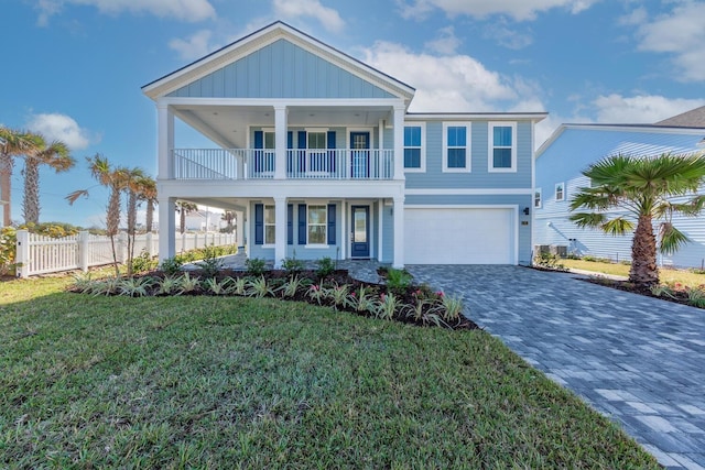 coastal inspired home featuring a front yard, a balcony, fence, a garage, and decorative driveway