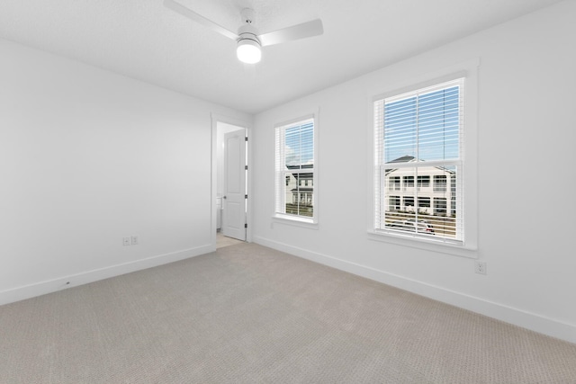 unfurnished room with a wealth of natural light, baseboards, light carpet, and a ceiling fan