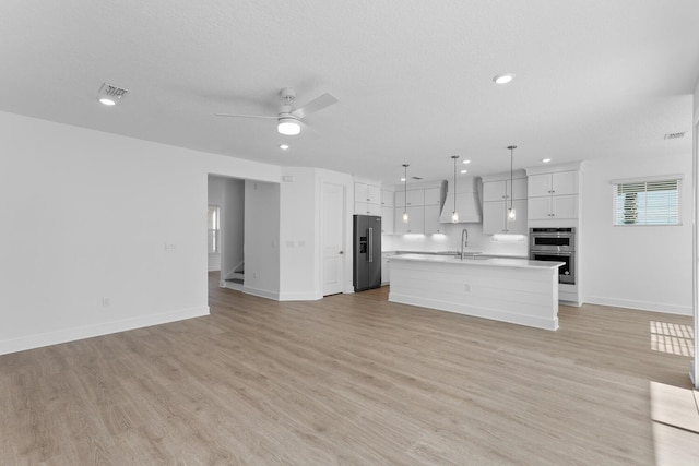 unfurnished living room featuring a sink, visible vents, light wood-style flooring, and a ceiling fan