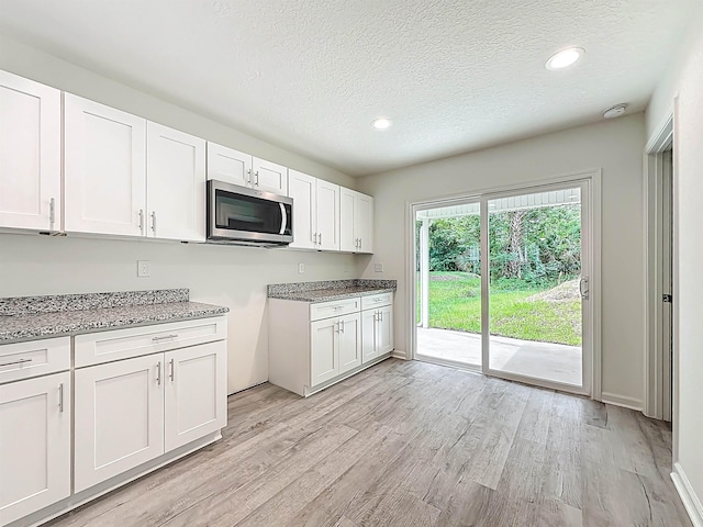 921 Helen St, Saint Augustine, FL 32084 - kitchen featuring stainless steel microwave, light wood-style flooring, white cabinets, a textured ceiling, and light stone countertops