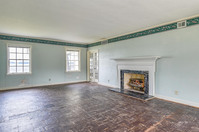 unfurnished living room featuring french doors, dark parquet flooring, a wealth of natural light, and a premium fireplace