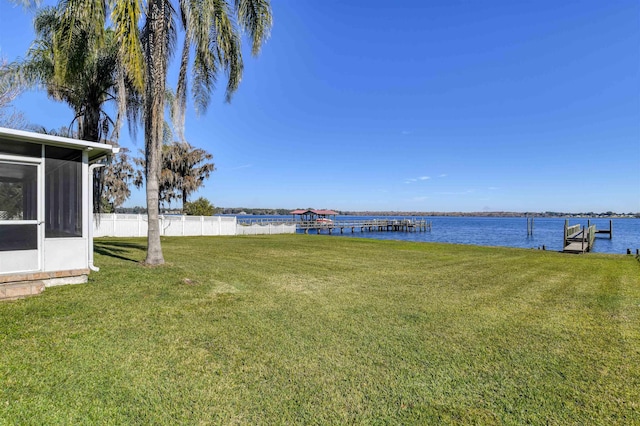 view of yard featuring a sunroom, a water view, and a dock