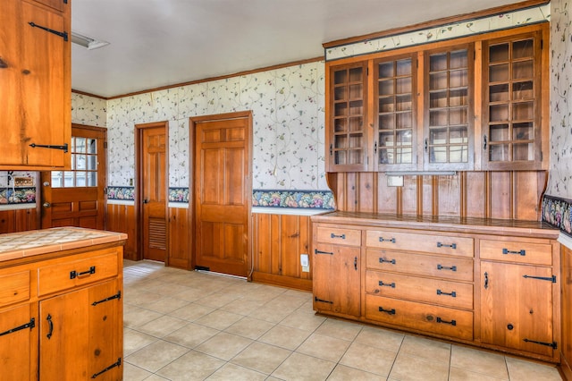 kitchen featuring tile countertops, crown molding, wooden walls, and light tile patterned floors