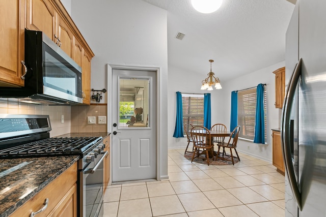 kitchen with decorative backsplash, appliances with stainless steel finishes, dark stone counters, an inviting chandelier, and light tile patterned flooring