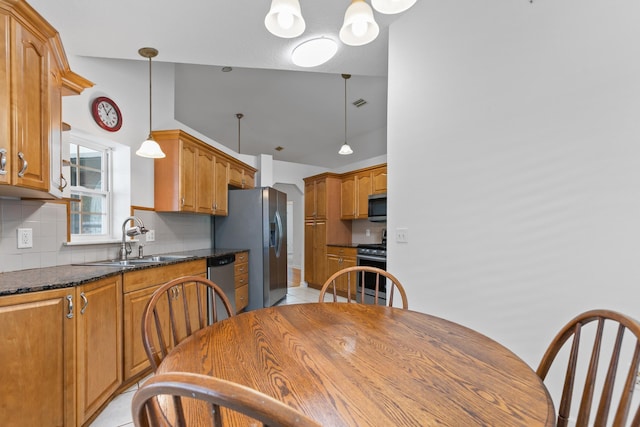 kitchen featuring decorative backsplash, stainless steel appliances, sink, dark stone countertops, and hanging light fixtures