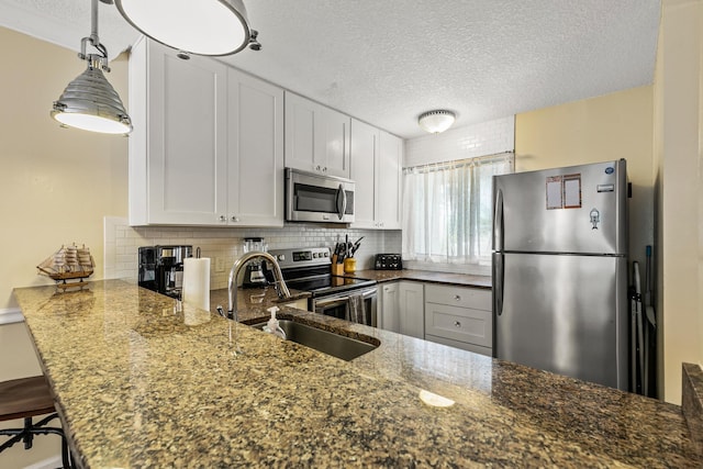 kitchen with white cabinetry, kitchen peninsula, dark stone counters, a textured ceiling, and appliances with stainless steel finishes