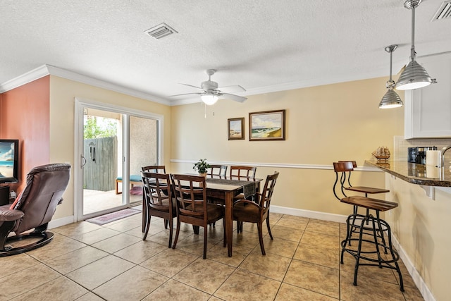 tiled dining room with a textured ceiling, ceiling fan, and ornamental molding