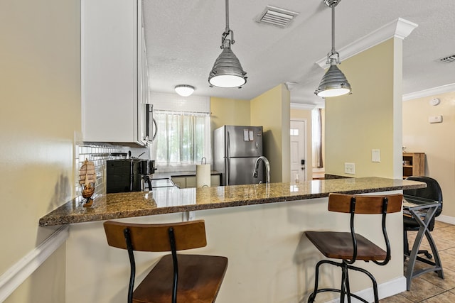 kitchen with stainless steel appliances, hanging light fixtures, kitchen peninsula, dark stone counters, and a breakfast bar area