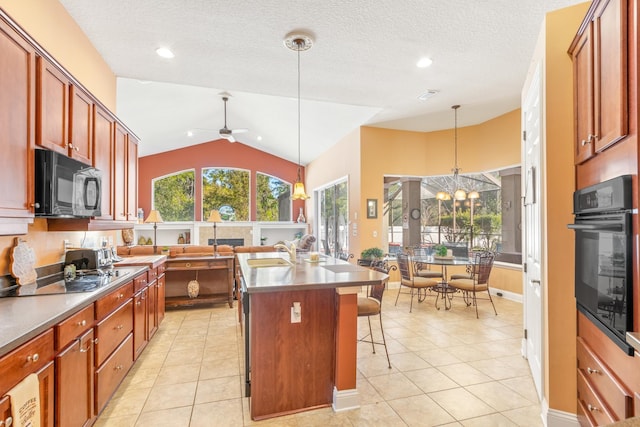 kitchen featuring an island with sink, lofted ceiling, hanging light fixtures, a breakfast bar, and black appliances