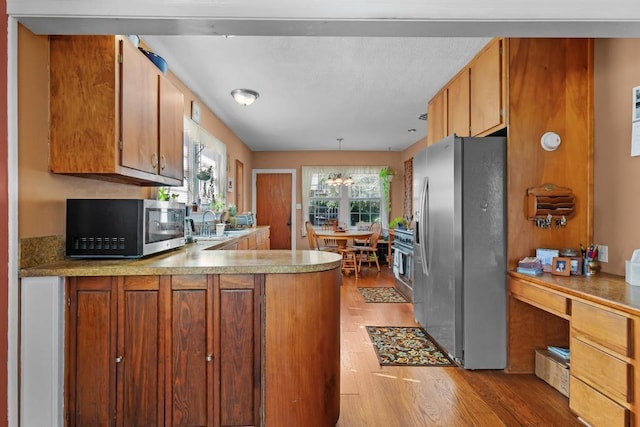 kitchen with kitchen peninsula, a wealth of natural light, light hardwood / wood-style flooring, and appliances with stainless steel finishes