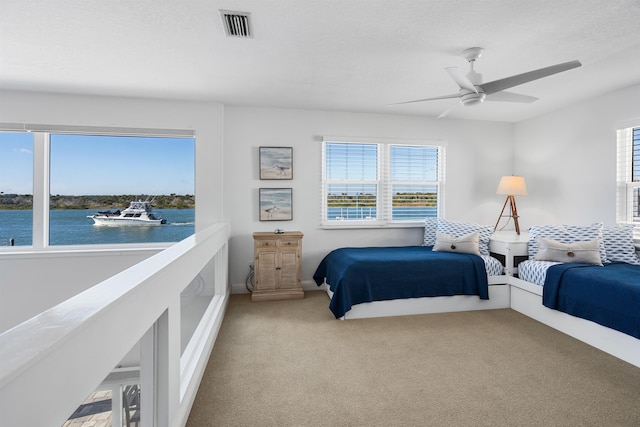 bedroom with a textured ceiling, a water view, a ceiling fan, visible vents, and carpet