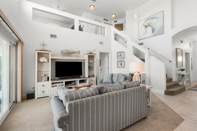 living room featuring arched walkways, stairway, a towering ceiling, and visible vents