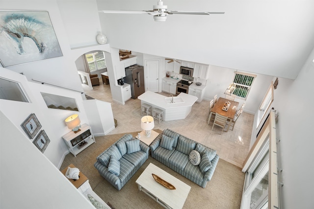 living area with light carpet, a high ceiling, arched walkways, and a ceiling fan