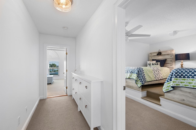 hall featuring light carpet, a textured ceiling, and baseboards