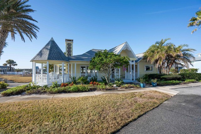 victorian house featuring covered porch, a chimney, and a front yard