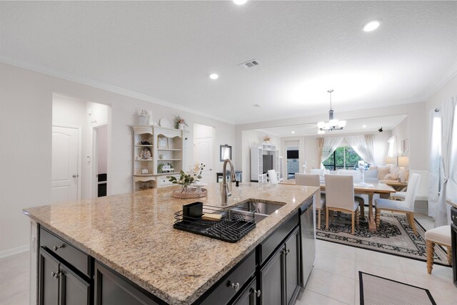 kitchen with an island with sink, ornamental molding, open floor plan, an inviting chandelier, and stainless steel dishwasher