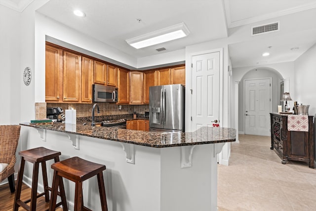 kitchen featuring a breakfast bar, backsplash, dark stone countertops, kitchen peninsula, and stainless steel appliances