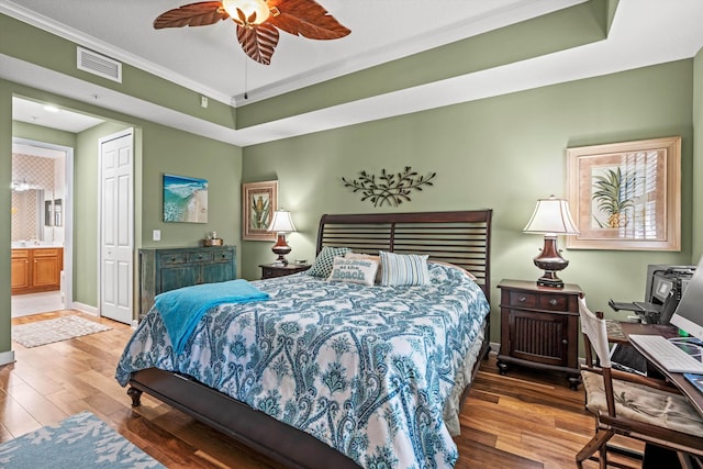 bedroom featuring connected bathroom, hardwood / wood-style flooring, ceiling fan, and crown molding