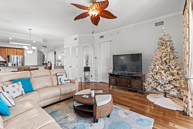 living room with light hardwood / wood-style floors, ceiling fan with notable chandelier, and ornamental molding