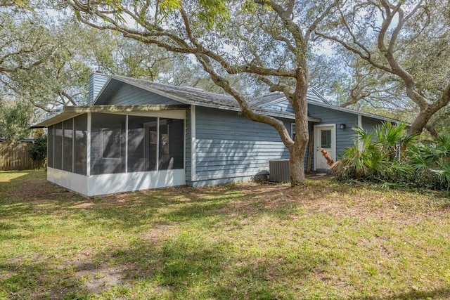 back of property with central AC unit, a lawn, a sunroom, and a chimney