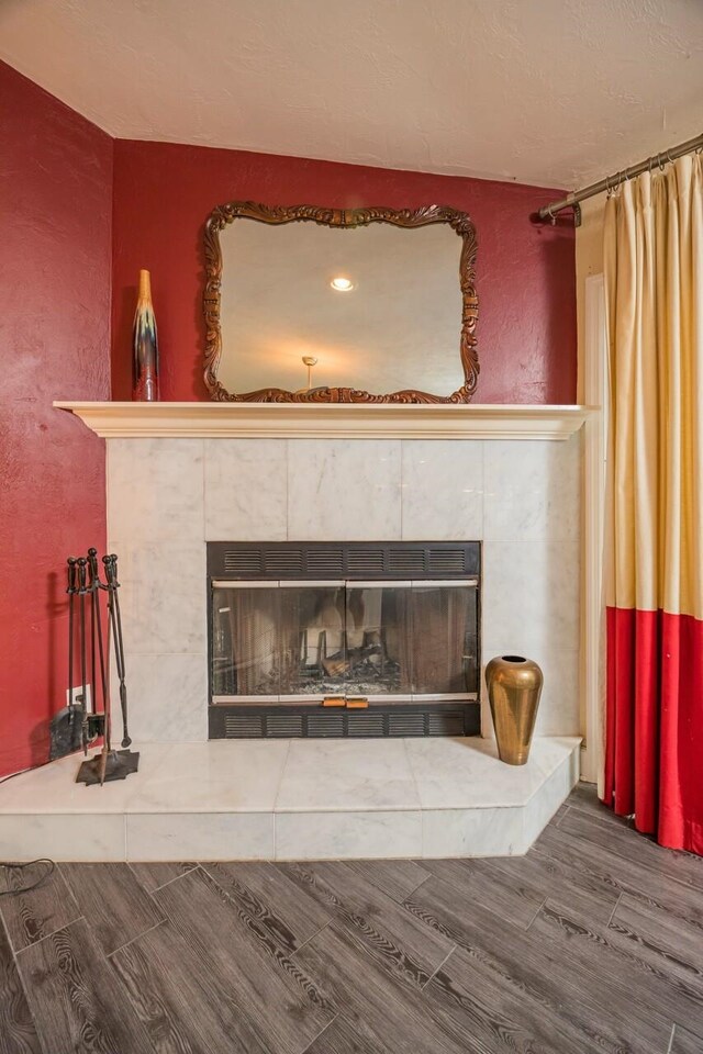 interior details featuring a tiled fireplace, a textured wall, and wood finish floors