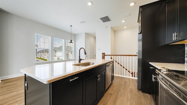 kitchen with sink, an island with sink, light hardwood / wood-style floors, decorative light fixtures, and appliances with stainless steel finishes