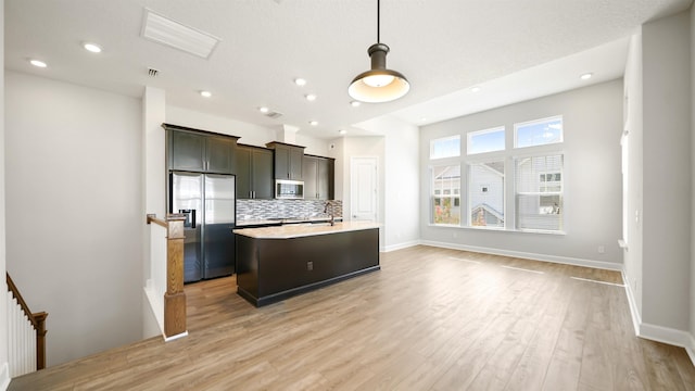 kitchen featuring tasteful backsplash, dark brown cabinets, stainless steel appliances, a center island with sink, and light hardwood / wood-style floors