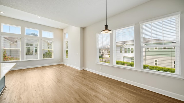 unfurnished dining area with a textured ceiling, light hardwood / wood-style flooring, and a healthy amount of sunlight