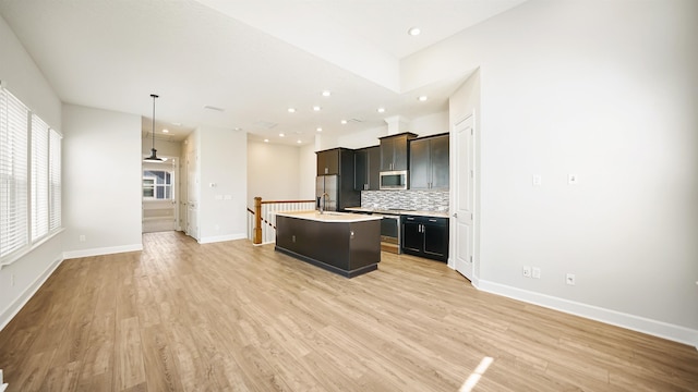 kitchen with stainless steel appliances, backsplash, pendant lighting, light hardwood / wood-style floors, and a center island with sink