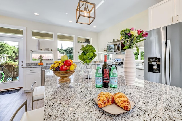 kitchen with white cabinetry, hardwood / wood-style flooring, light stone countertops, and appliances with stainless steel finishes