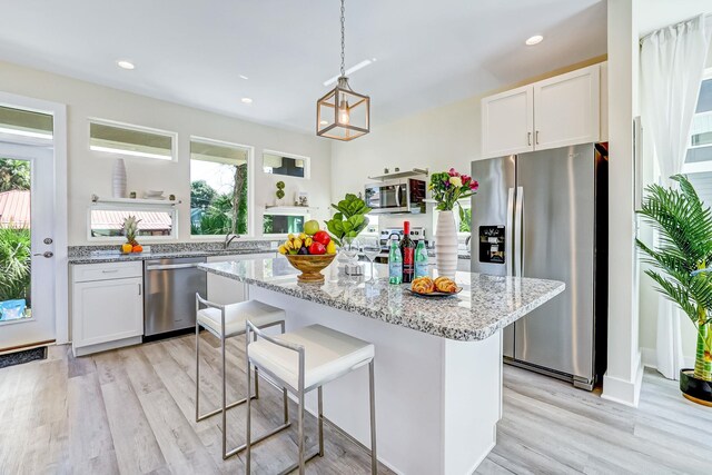 kitchen with light stone countertops, stainless steel appliances, decorative light fixtures, white cabinets, and light hardwood / wood-style floors