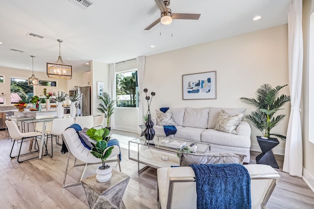 living room with ceiling fan with notable chandelier and light hardwood / wood-style flooring