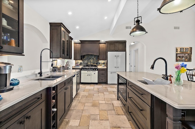 kitchen with built in appliances, custom range hood, hanging light fixtures, and sink