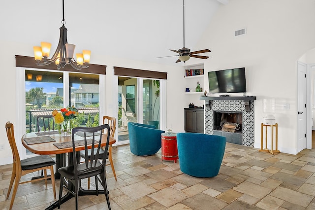 dining area featuring high vaulted ceiling, a tiled fireplace, and ceiling fan with notable chandelier