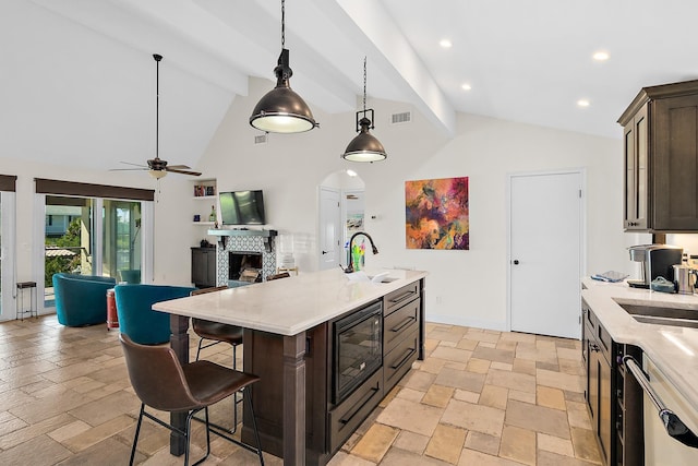 kitchen with a center island with sink, a kitchen breakfast bar, pendant lighting, dark brown cabinetry, and beamed ceiling