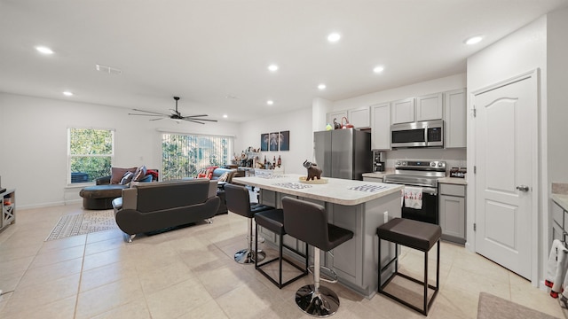 kitchen featuring gray cabinetry, a kitchen bar, a center island, ceiling fan, and stainless steel appliances