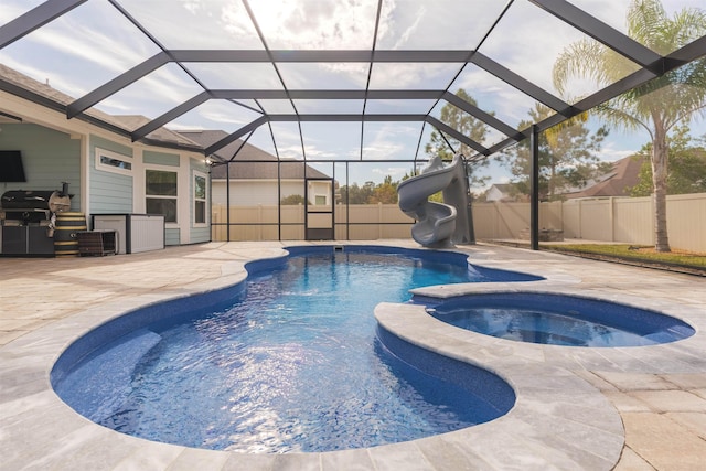 view of swimming pool with a patio, a pool with connected hot tub, grilling area, a water slide, and a fenced backyard