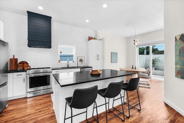 kitchen featuring electric range, a breakfast bar, a sink, white cabinets, and dark countertops