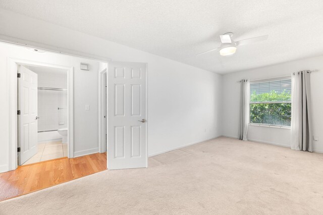 unfurnished bedroom featuring ceiling fan, ensuite bath, carpet floors, a textured ceiling, and baseboards